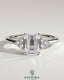 Kynora CJ 2ct emerald claw solitaire engagement ring with round shoulder stones, featuring a central emerald cut gemstone and delicate band