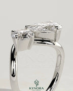 Kynora CJ Toi et Moi engagement ring with 1ct round and 1.5ct pear-shaped diamonds on wave band, showcasing intricate design.