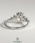 Kynora CJ 2ct oval claw solitaire engagement ring with clustered round shoulder stones, three-stone design, elegant jewelry piece.