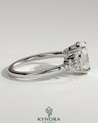 Kynora CJ three-stone engagement ring featuring a 2-carat oval claw solitaire with clustered round shoulder stones.