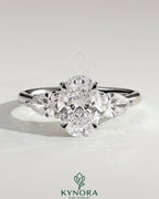 Kynora CJ 2ct oval claw trilogy engagement ring with pear side stones and open trellis gallery design, showcasing intricate craftsmanship.