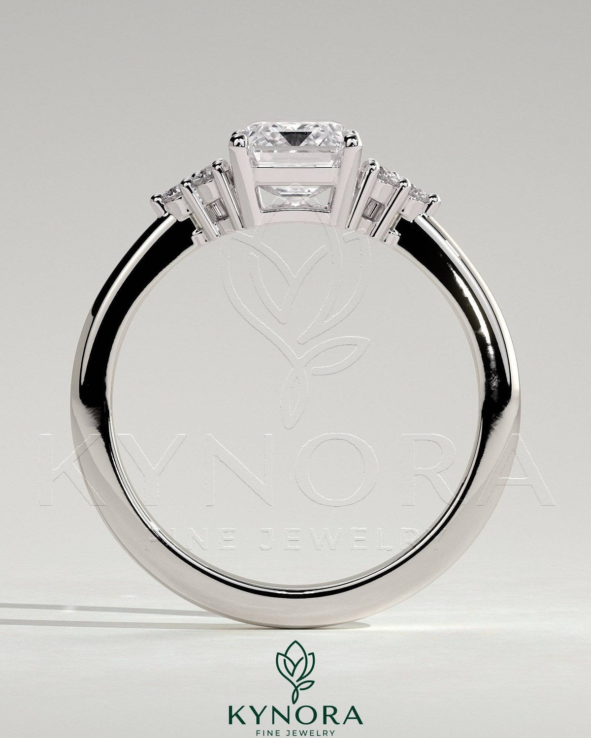 Kynora CJ 2ct emerald claw solitaire engagement ring with round shoulder stones, featuring a central emerald cut gemstone.