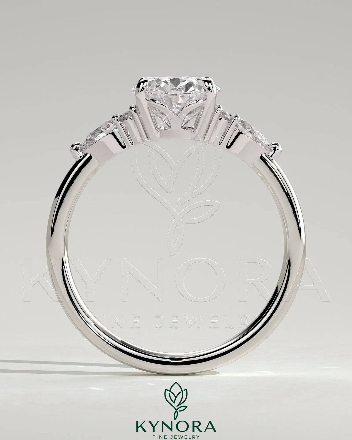 Kynora CJ 2ct oval claw solitaire engagement ring with pear-shaped accents and round shoulder stones, elegant three-stone design.