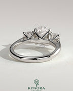 Kynora CJ 2ct oval claw trilogy engagement ring with round side stones, open trellis gallery, tapered band, and intricate design.