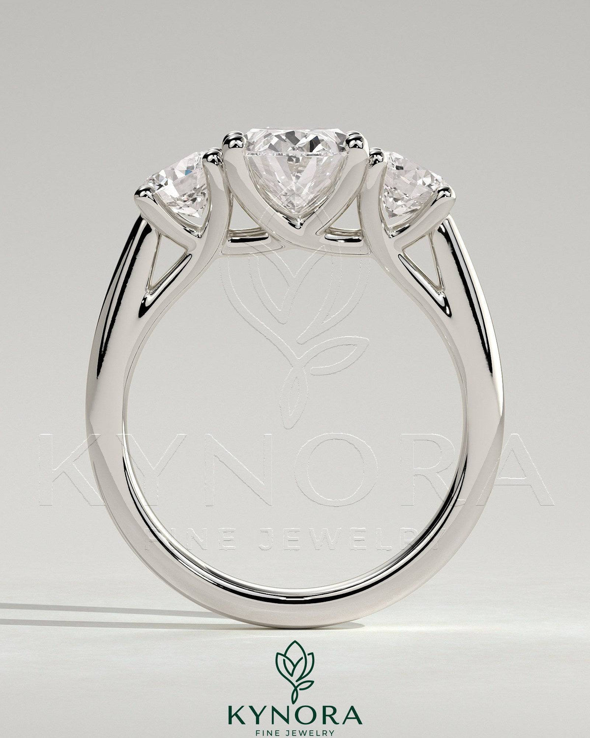 Kynora CJ 2ct oval claw trilogy engagement ring with round side stones, open trellis gallery, tapered band, three-stone design.