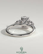Kynora CJ 2ct elongated cushion claw trilogy engagement ring with round side stones and delicate lily detail.