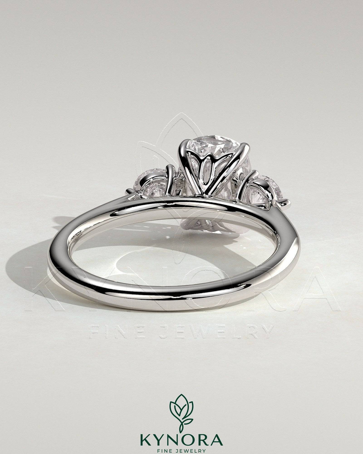 Kynora CJ 2ct elongated cushion claw trilogy engagement ring with round side stones and delicate lily detail.