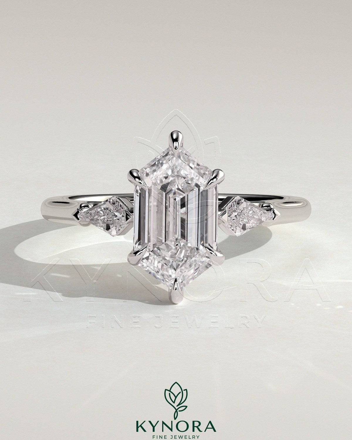 Kynora CJ 2ct elongated hexagon claw trilogy engagement ring with kite side stones, featuring three-stone design and intricate detailing. Imagen principal del producto