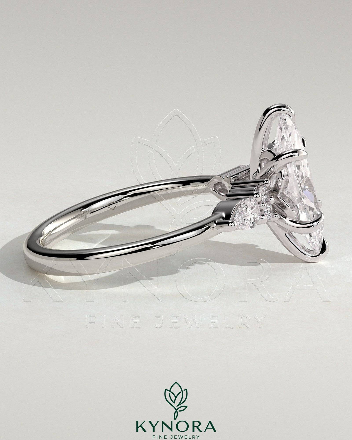 Kynora CJ three-stone engagement ring featuring a 2ct marquise claw solitaire with pear-shaped and round shoulder accent stones.