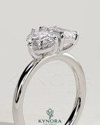 Kynora CJ Toi et Moi engagement ring featuring a 1.5ct pear-shaped diamond and 1.8ct emerald gemstone in a claw setting.