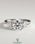 Kynora CJ 2ct round claw trilogy engagement ring with pear side stones and open trellis gallery design.