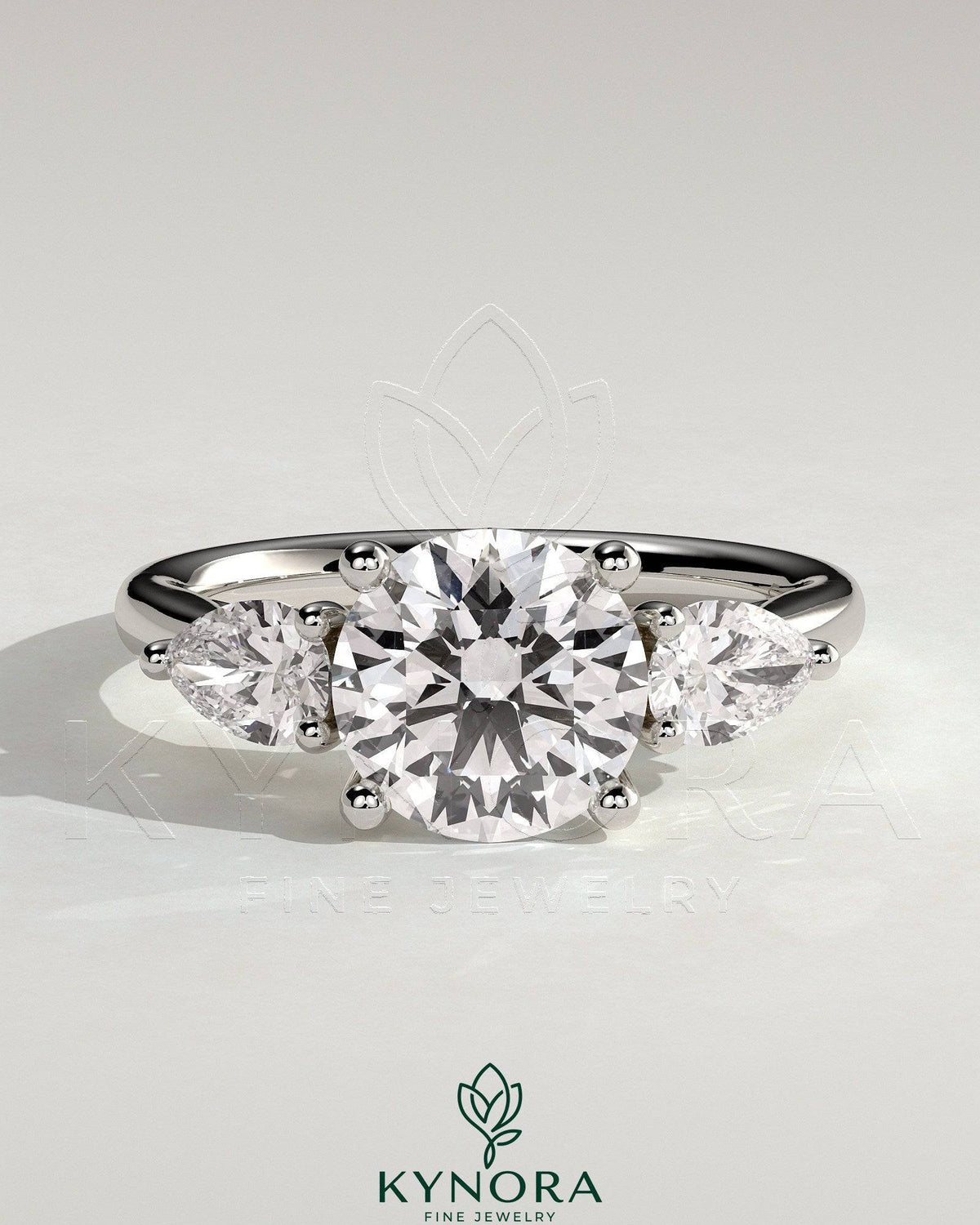 Kynora CJ 2ct round claw trilogy engagement ring with pear side stones and open trellis gallery design.