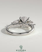 Kynora CJ 2ct round claw trilogy engagement ring with pear side stones and open trellis gallery design.