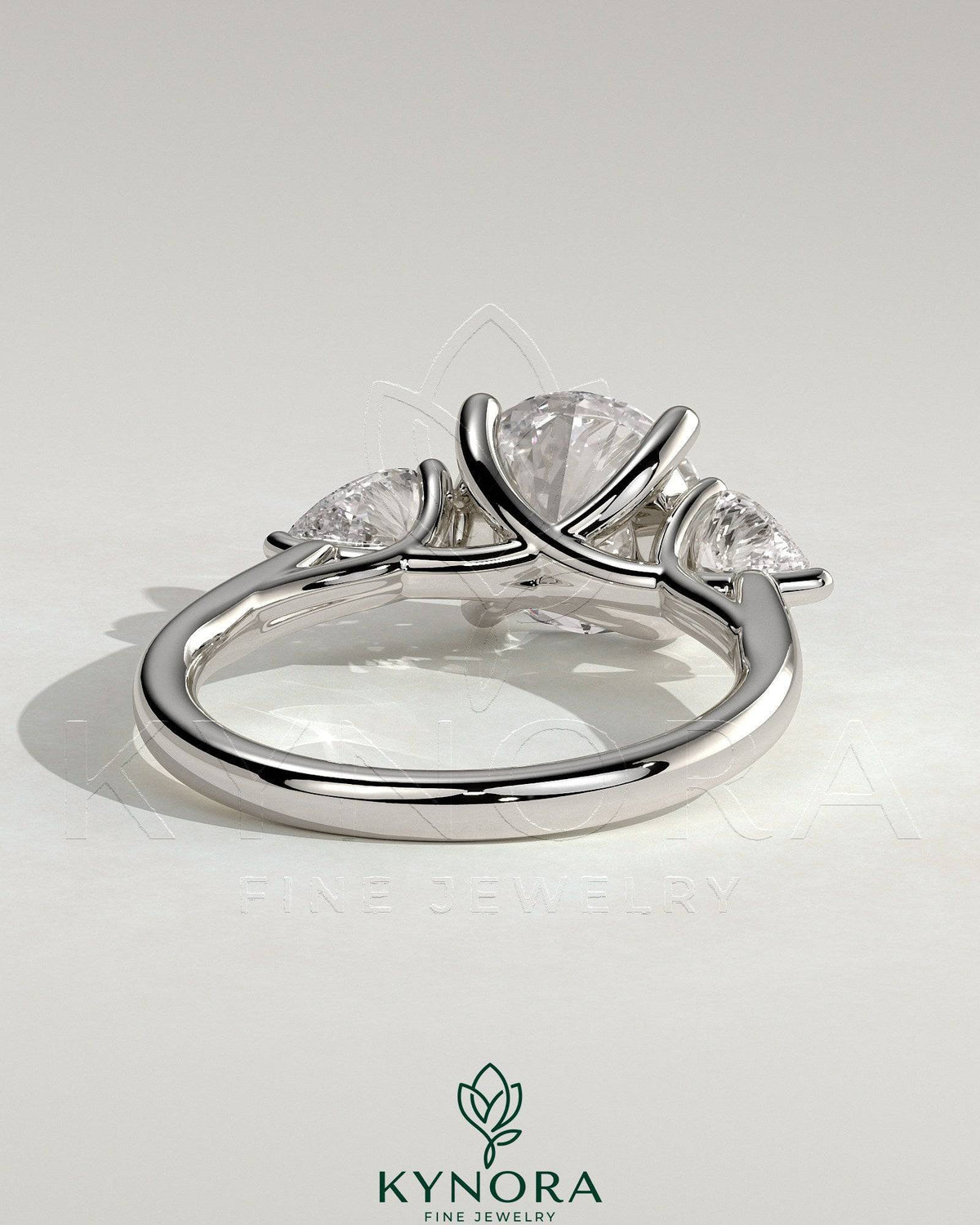Kynora CJ 2ct round claw trilogy engagement ring with pear side stones and open trellis gallery design.
