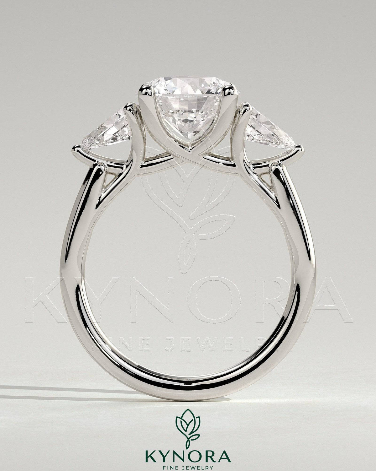 Kynora CJ 2ct three-stone engagement ring with round claw set center stone, pear side stones, and open trellis gallery design.