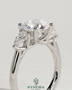 Kynora CJ 2ct round claw trilogy engagement ring with pear side stones and open trellis gallery setting.
