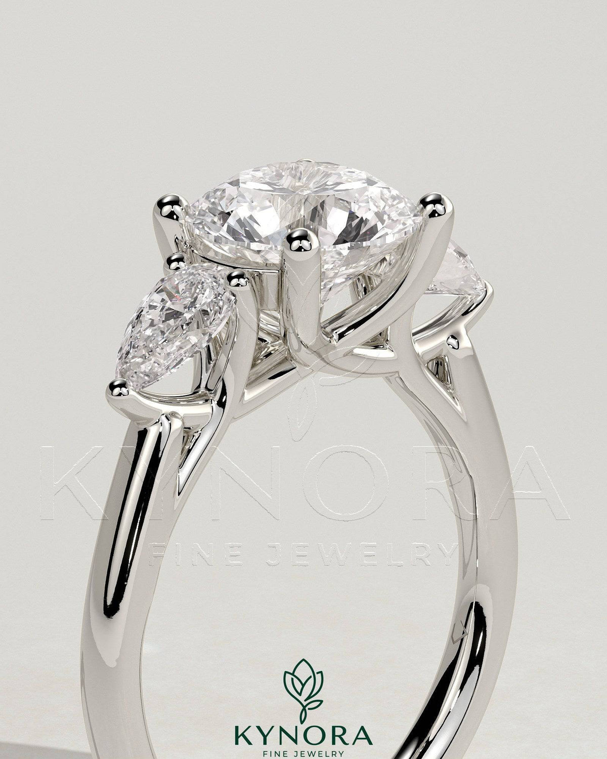 Kynora CJ 2ct round claw trilogy engagement ring with pear side stones and open trellis gallery setting.