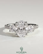 Kynora CJ 2ct oval claw trilogy engagement ring with round side stones, pave band, and trellis gallery design.