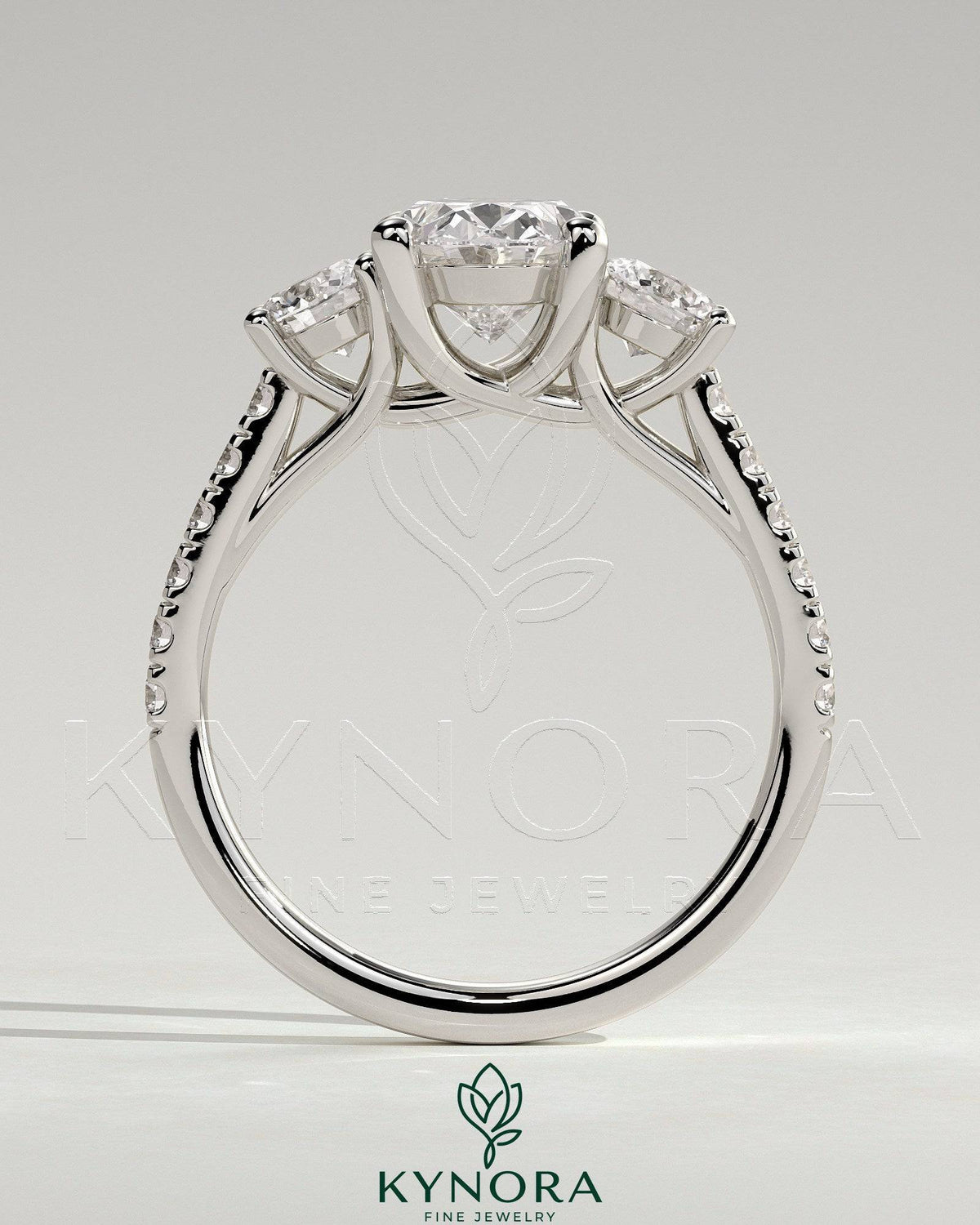 Kynora CJ three stone engagement ring with 2ct oval center, round side stones, pave band, and trellis gallery design.
