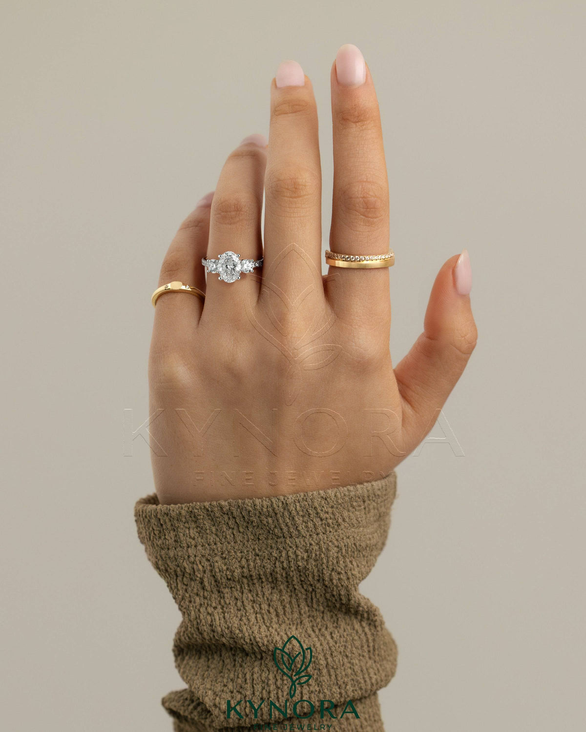 Kynora CJ three-stone engagement ring featuring a 2ct oval claw trilogy center stone with round side stones and pave band.