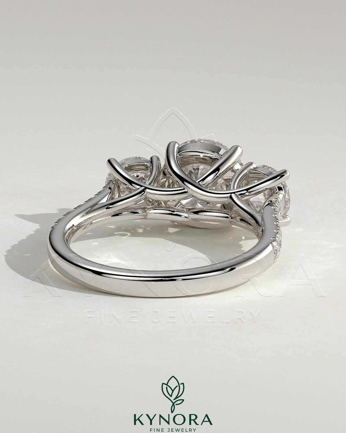 Kynora CJ three-stone engagement ring with 2ct round claw trilogy center, side stones, pave band, and trellis gallery design.