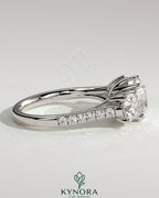 Kynora CJ three-stone engagement ring featuring a 2ct round claw trilogy center stone with round side stones, pave band, and trellis gallery design.