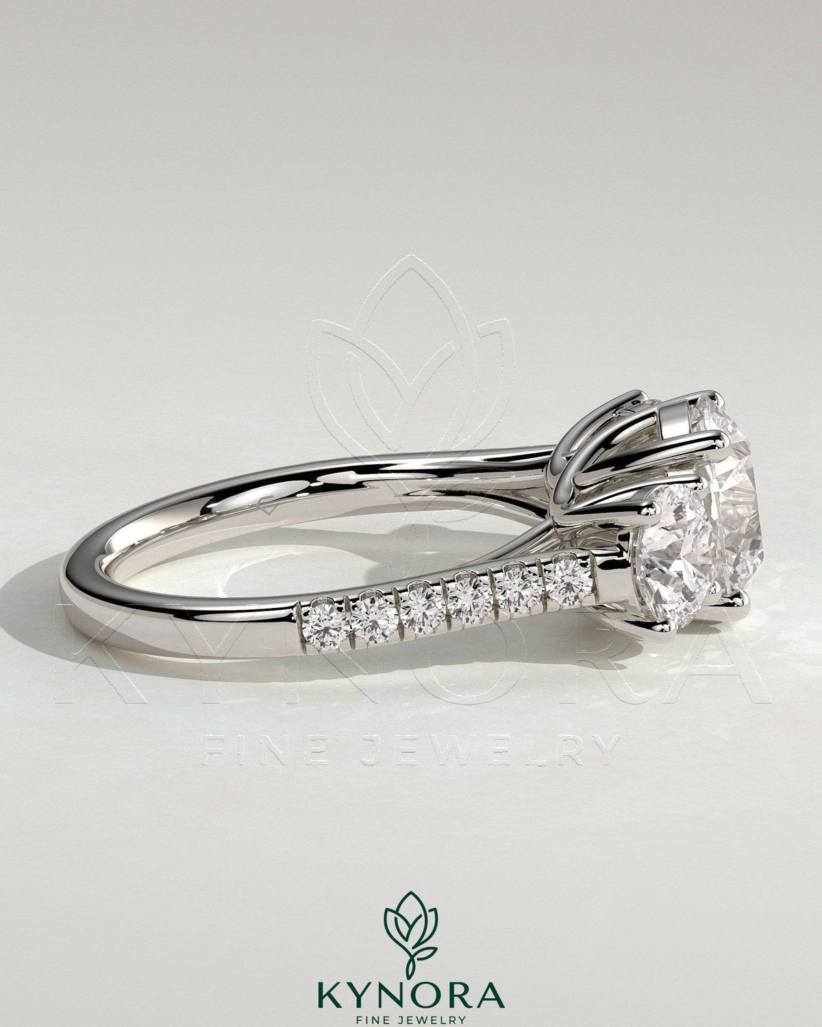 Kynora CJ three-stone engagement ring featuring a 2ct round claw trilogy center stone with round side stones, pave band, and trellis gallery design.