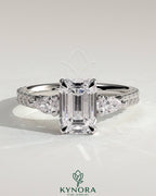 Kynora CJ 2ct emerald claw trilogy engagement ring with pear side stones and pave band, showcasing sparkling fine jewelry.