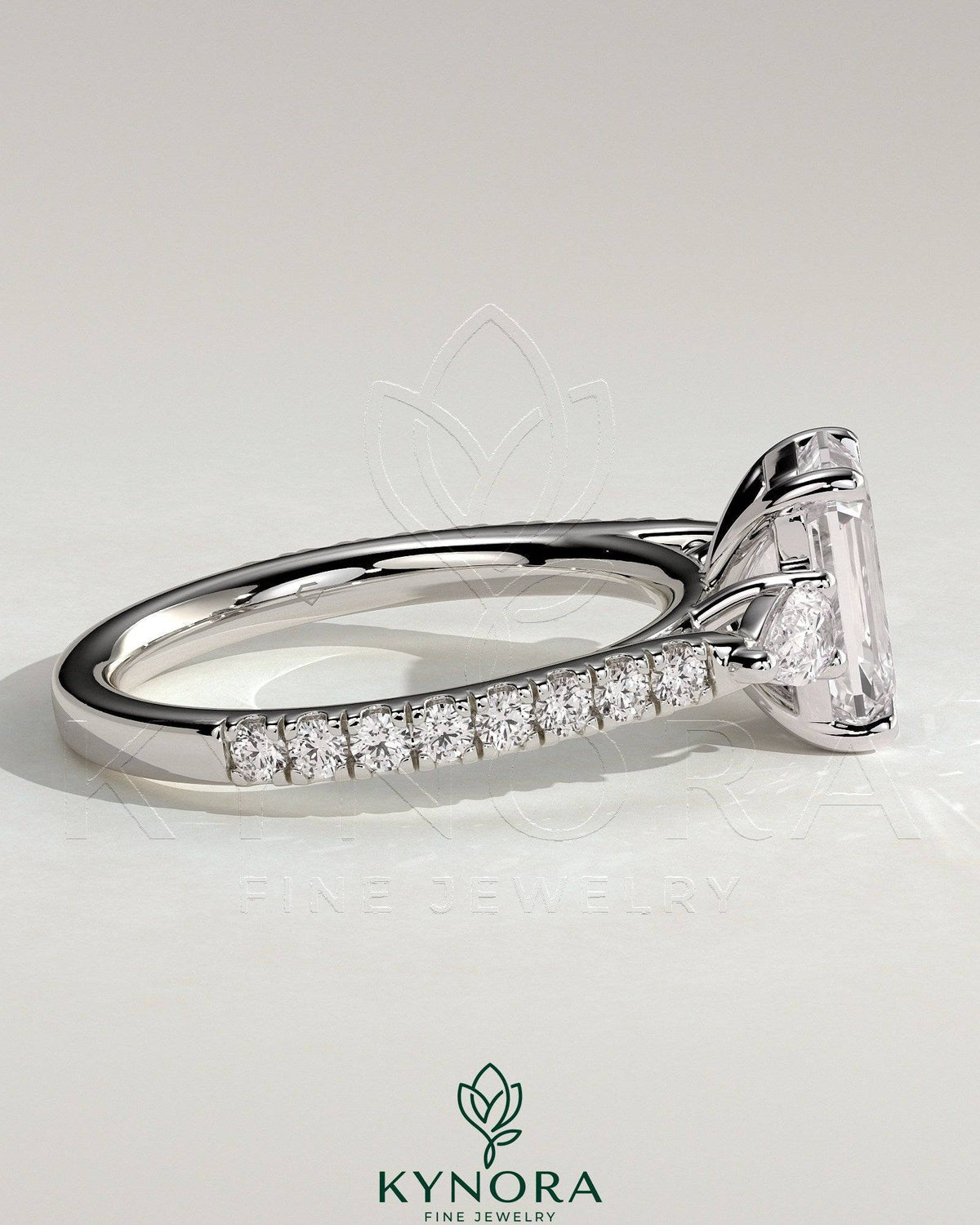 Kynora CJ 2ct emerald claw trilogy engagement ring with pear side stones and pave band, showcasing sparkling diamond accents.