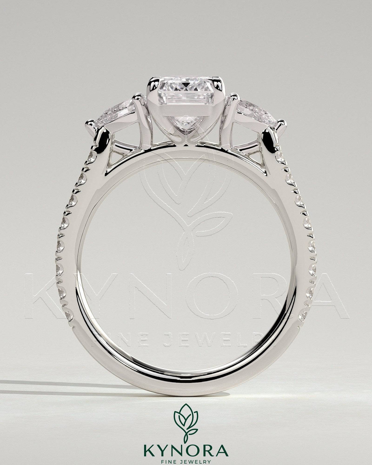 Kynora CJ 2ct emerald claw trilogy engagement ring with pear side stones and pave band, showcasing elegant diamond craftsmanship.