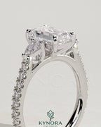 Kynora CJ 2ct emerald claw trilogy engagement ring with pear side stones and pave band, showcasing intricate design and sparkling gemstones.