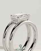 Kynora CJ 2ct emerald east-west claw solitaire engagement ring with a spaced double band, showcasing a stunning emerald gemstone.