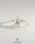 Pear cut moissanite half-bezel engagement ring in 925 silver with a sleek design on an ivory backdrop.
