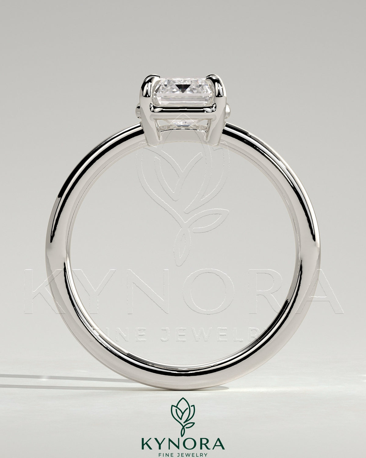 Kynora CJ 2ct emerald claw solitaire engagement ring with bezel frame, featuring a vibrant green emerald gemstone and sleek metal band.