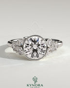 Kynora CJ 2ct round bezel solitaire engagement ring with clustered round and marquise shoulder stones in a detailed jewelry image.