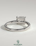 Kynora CJ 2ct emerald cut east-west claw solitaire engagement ring with raised basket gallery showcasing a stunning emerald gemstone.
