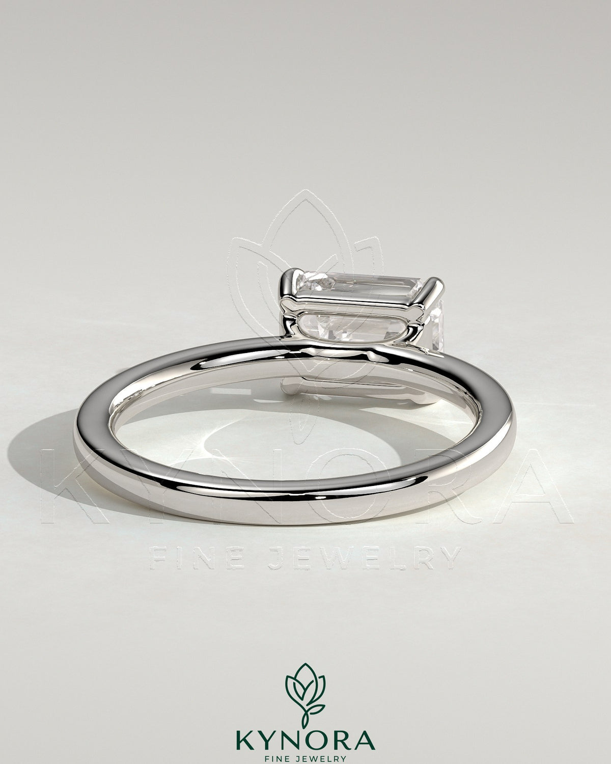 Kynora CJ 2ct emerald cut east-west claw solitaire engagement ring with raised basket gallery showcasing a stunning emerald gemstone.