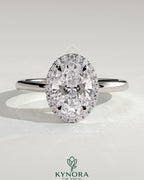 Kynora CJ 2ct oval claw solitaire engagement ring with halo of smaller diamonds, showcasing elegant design and sparkling center stone.
