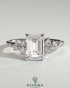 Kynora CJ 2ct emerald claw solitaire engagement ring with round cluster shoulder stones, showcasing elegant design and sparkling gemstones.