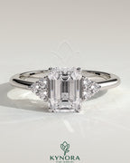 Kynora CJ 2ct emerald claw solitaire engagement ring with round shoulder stones, featuring a central emerald cut gemstone and delicate band