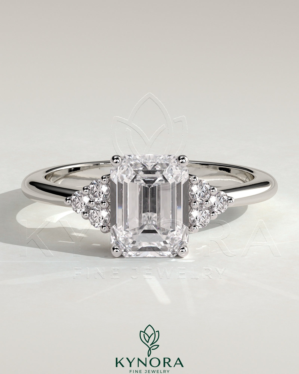 Kynora CJ 2ct emerald claw solitaire engagement ring with round shoulder stones, featuring a central emerald cut gemstone and delicate band