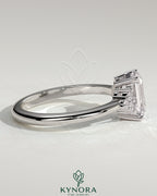 Kynora CJ 2ct emerald claw solitaire engagement ring with round shoulder stones, featuring a central emerald cut gemstone and side accents.