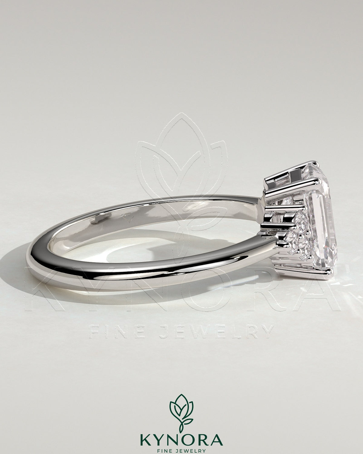 Kynora CJ 2ct emerald claw solitaire engagement ring with round shoulder stones, featuring a central emerald cut gemstone and side accents.