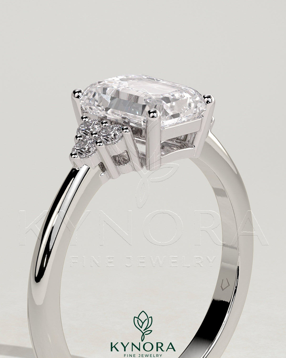 Kynora CJ 2ct emerald claw solitaire engagement ring with round shoulder stones, featuring a prominent central emerald cut gemstone.