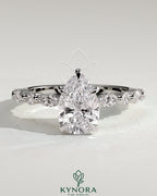 Kynora CJ 2ct pear-shaped diamond solitaire engagement ring with marquise and round accent stones on a silver band.