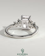 Kynora CJ 2ct radiant claw solitaire engagement ring with clustered round shoulder stones, featuring a sparkling central diamond.