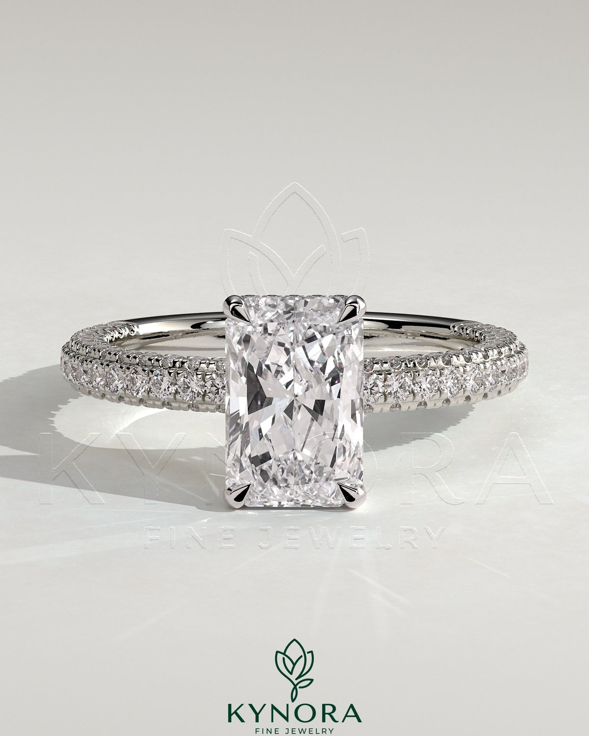 Kynora CJ 2ct radiant claw solitaire engagement ring with hidden halo and triple pave band, featuring sparkling diamond details.