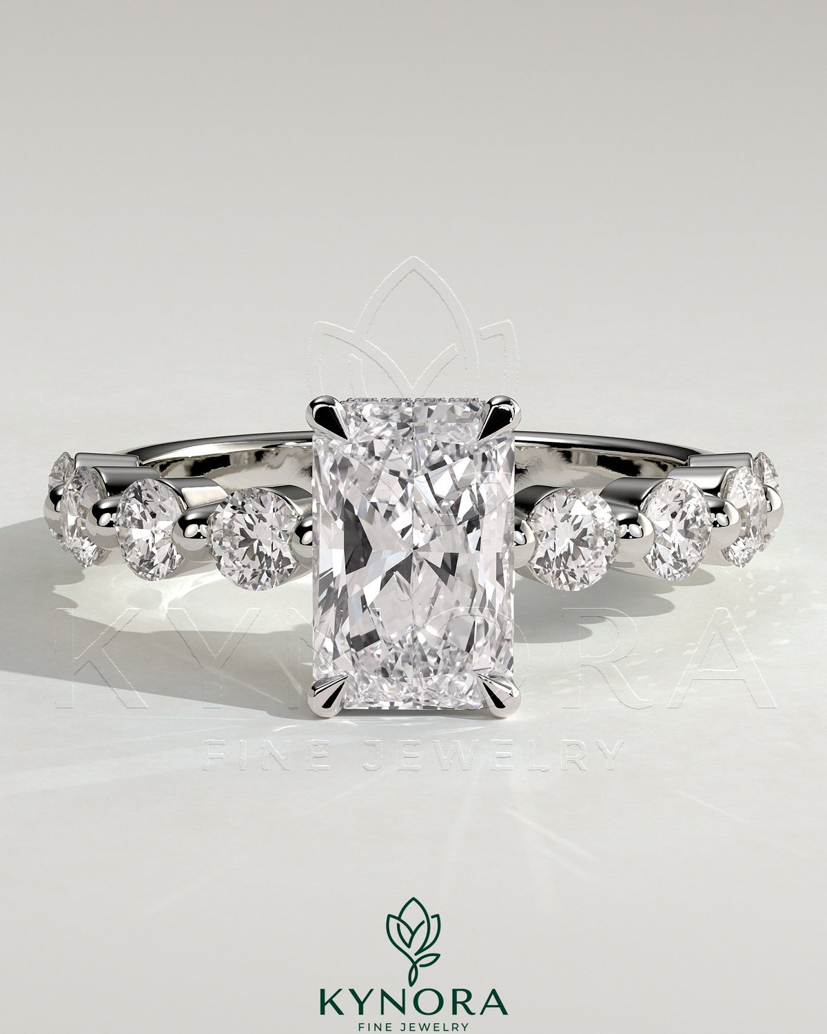 Kynora CJ 2ct radiant claw solitaire engagement ring with round accent stones and hidden halo design.