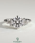 Kynora CJ 2ct round claw solitaire engagement ring with clustered round shoulder stones, showcasing a sparkling diamond design.