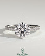 Kynora CJ 2ct round diamond solitaire engagement ring with claw setting, crown gallery, and pave band, showcasing elegant jewelry design.